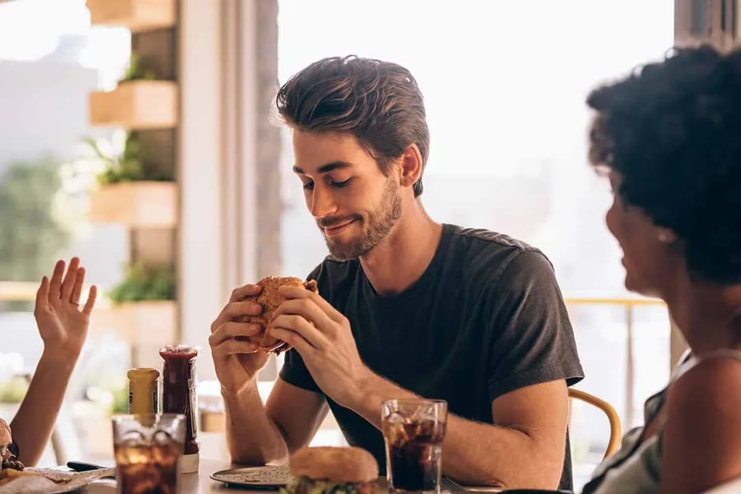 homme souriant dégustant un hamburger à table entouré d'amis et de boissons