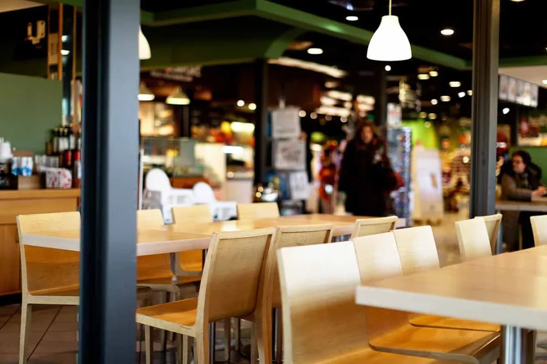 tables et chaises en bois vides dans une cafétéria avec personnes floues en arrière-plan