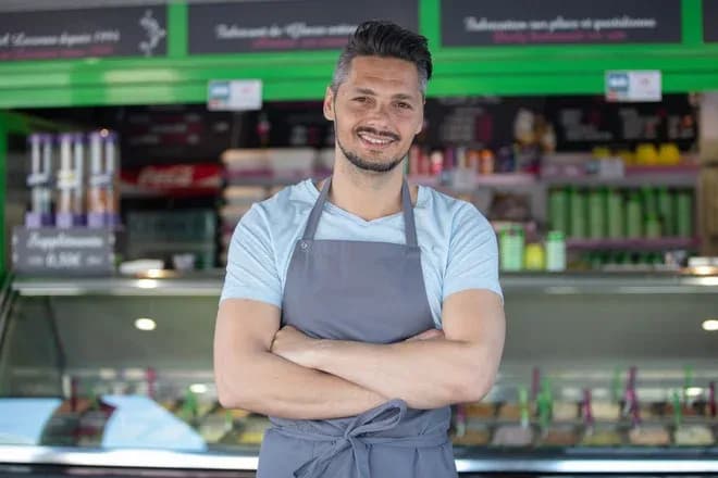 homme souriant en tablier devant un comptoir de glaces artisanales