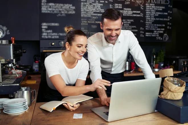 personnes souriantes travaillant ensemble sur un ordinateur dans un café moderne