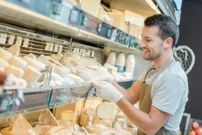 fromager en gants manipule des fromages dans une vitrine réfrigérée
