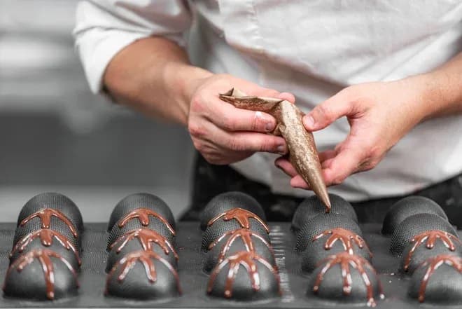 mains appliquent du chocolat fondu au cornet sur des dômes en chocolat