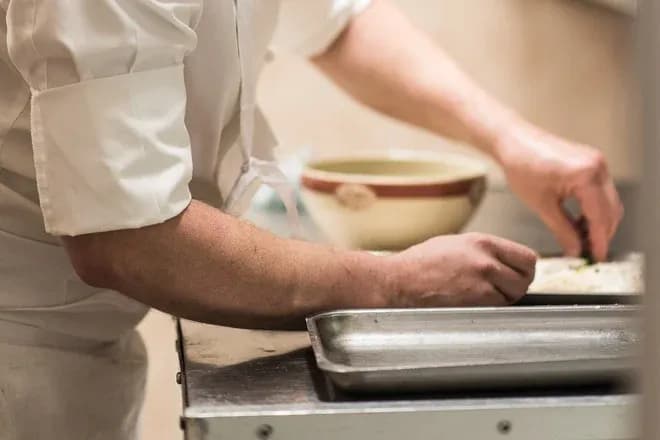mains d'un traiteur préparant des bouchées sur un plan de travail avec bol et plaque