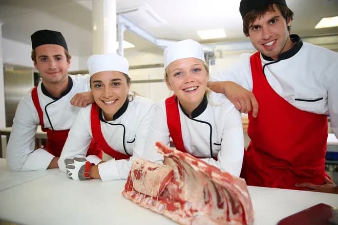 quatre jeunes en tenue de boucher souriants autour d'une pièce de viande