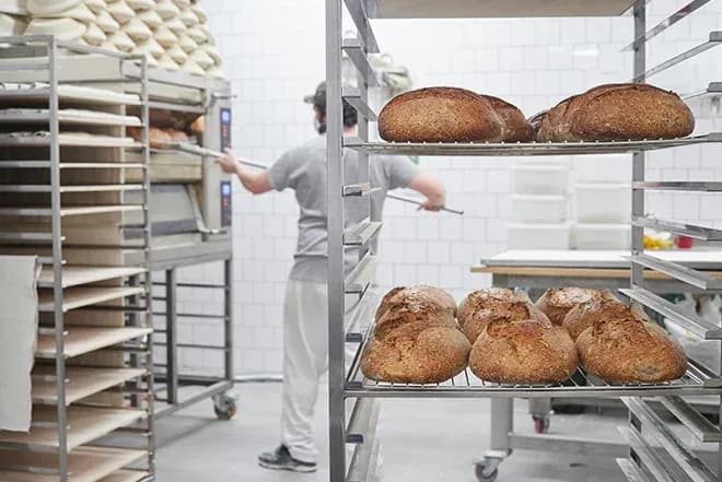 boulangerie avec du pain sur une étagère et un boulanger en arrière-plan en train de travailler