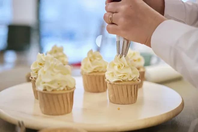 main d'un pâtissier décorant des cupcakes avec de la crème chantilly sur un plateau en bois