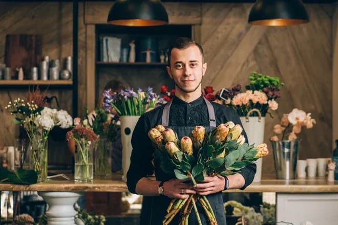 fleuriste tenant un bouquet de protéas dans une boutique remplie de fleurs