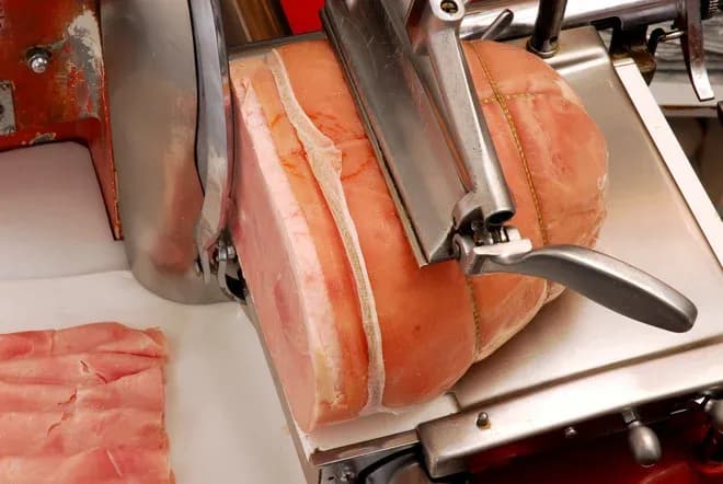 machine à trancher du jambon avec un morceau de viande en cours de découpe