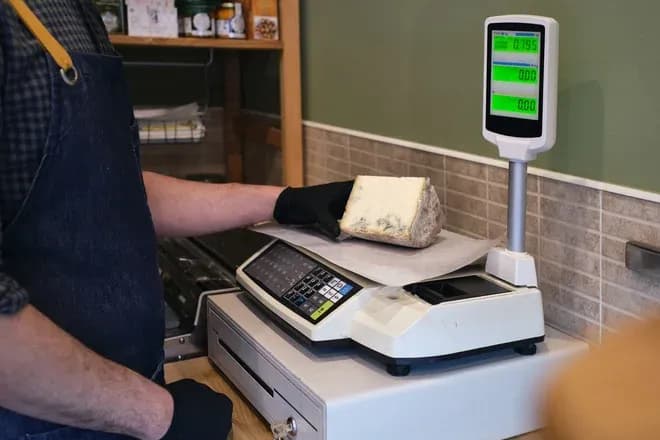 vendeur ganté posant un morceau de fromage persillé sur une balance