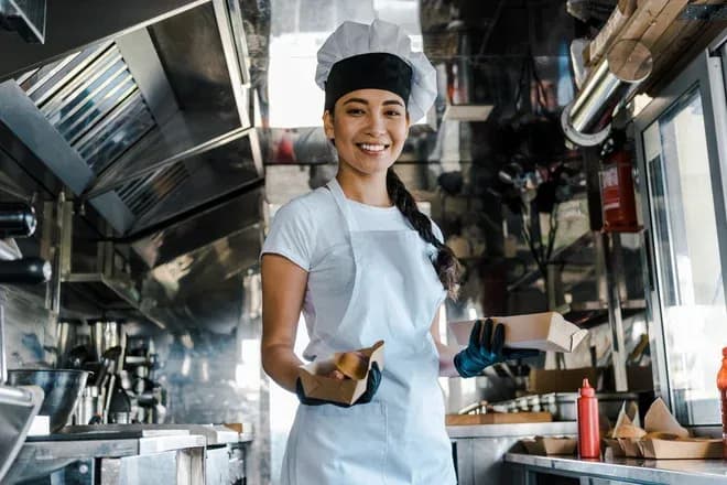 femme souriante en tenue de chef dans un camion de restauration rapide avec des plats à emporter