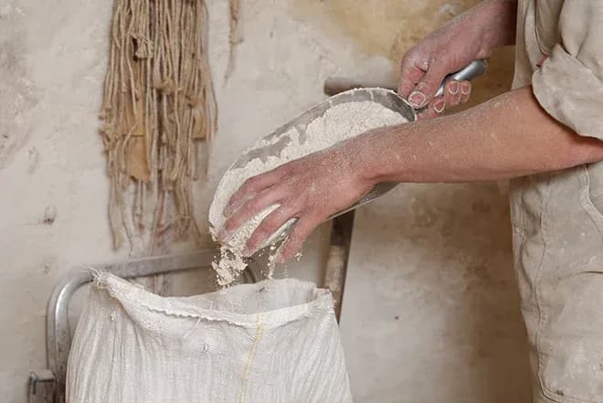 mains d'un meunier versant de la farine dans un sac