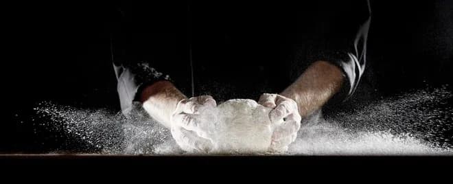 mains farinées pétrissant une boule de pâte avec nuage de farine