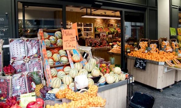 étal de primeur avec melons clémentines et fruits frais devant une boutique