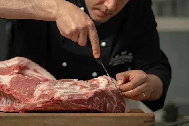 artisan boucher découpe de la viande sur une planche en bois avec un couteau