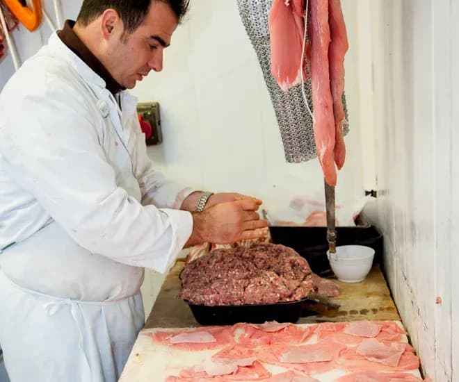 boucher préparant de la viande hachée dans un atelier avec des morceaux de viande sur la table