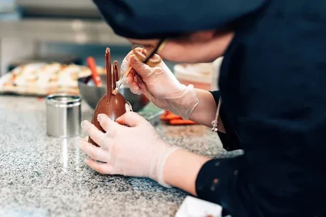 artisan chocolatier décorant un œuf en chocolat sur un plan de travail en cuisine