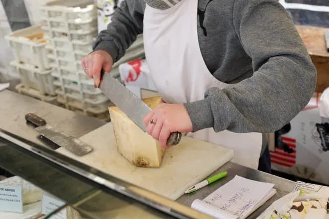 fromager coupant un fromage au couteau sur un comptoir