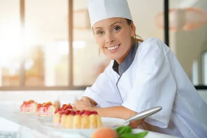 pâtissière souriante en tenue blanche devant entremets aux fruits