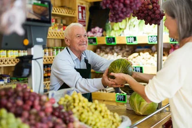 Vendeur souriant remettant une pastèque à une cliente dans un magasin de fruits et légumes