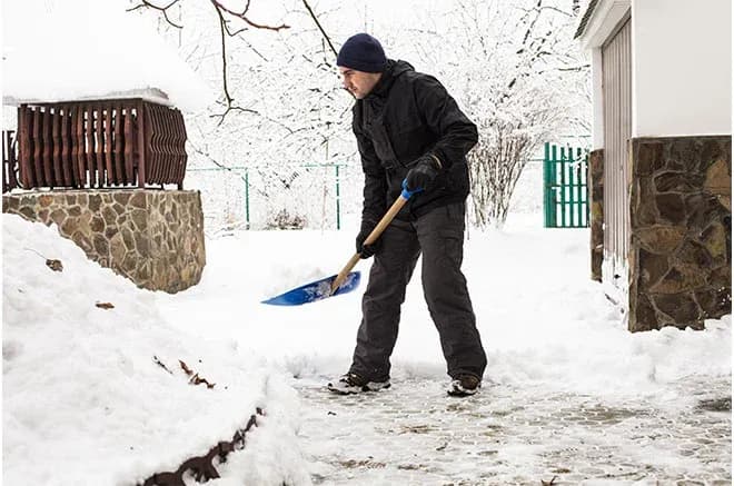 homme déblayant la neige d'une allée devant une maison