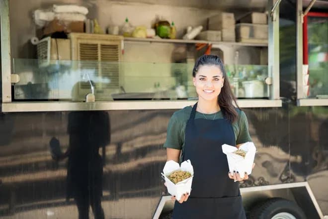 femme souriante tenant deux plats devant un food truck avec des ustensiles en arrière-plan