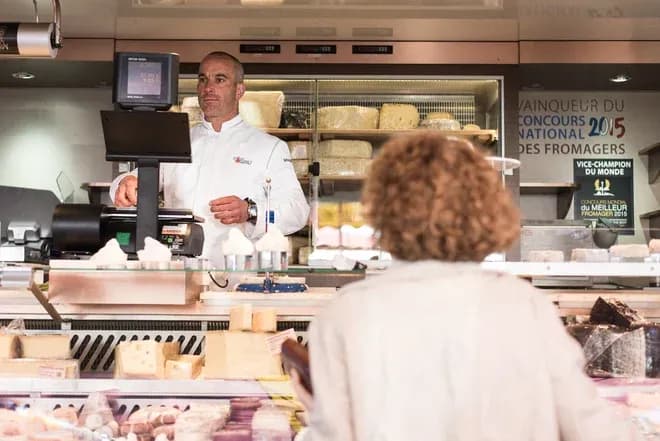 fromager en blouse blanche servant une cliente au comptoir de fromagerie