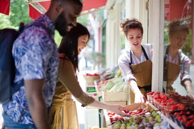 vendeuse aidant des clients à choisir fraises et pommes sur un stand de fruits