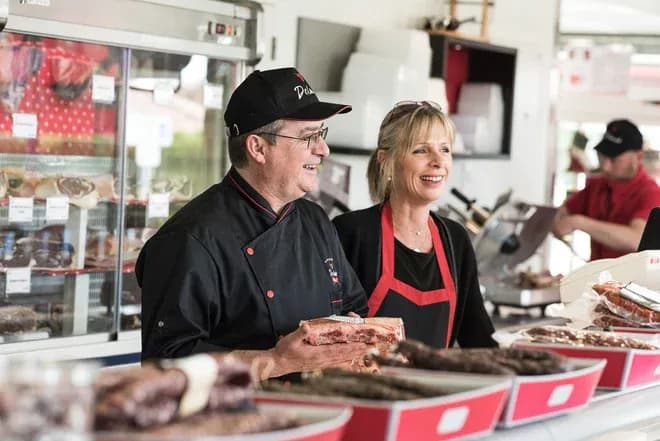 bouchers souriants derrière un comptoir présentant des pièces de viande