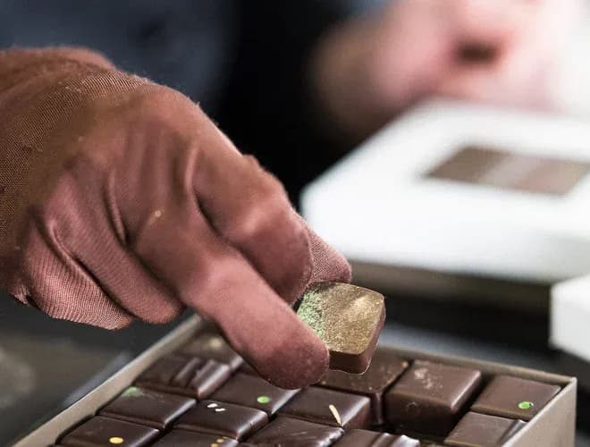 main gantée saisissant un chocolat carré dans une boîte
