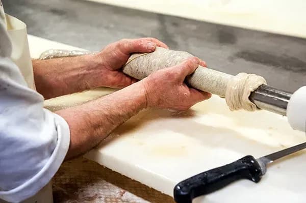 mains d'un charcutier remplissant un boyau de saucisse sur un poussoir