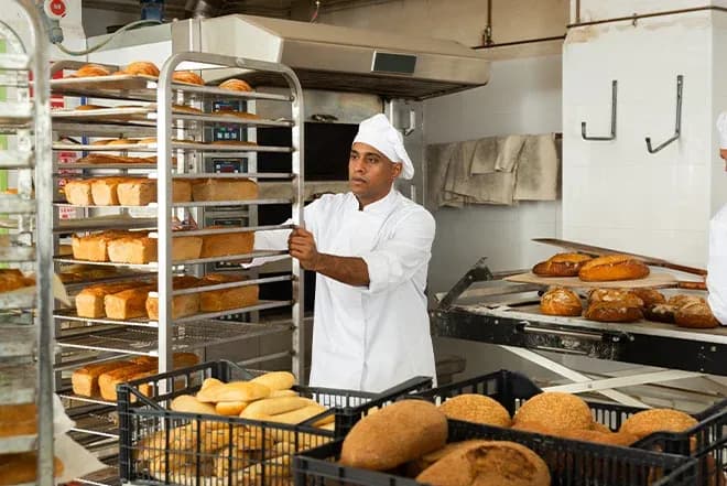 boulanger en tenue blanche poussant un chariot de pains