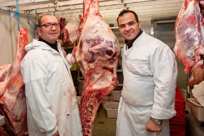 deux bouchers souriants posent avec une carcasse de viande dans une boucherie