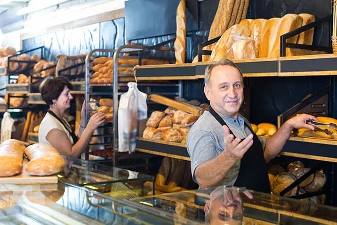 boulanger et boulangère dans une boulangerie entourés de pains frais sur des étagères