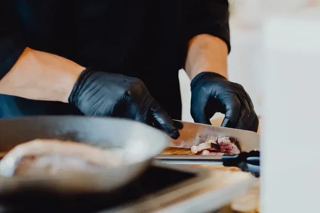 mains gantées noires coupant des tranches de viande cuite sur planche