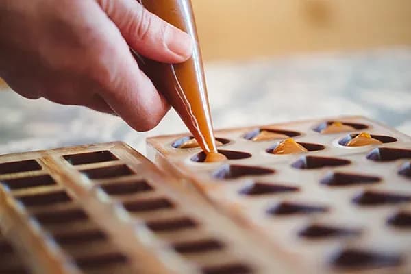 main dans une poche à douille remplie de chocolat verse le contenu dans un moule à bonbons