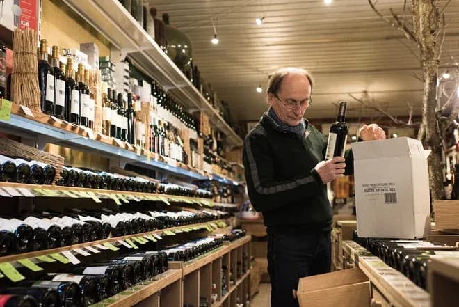 caviste range des bouteilles de vin dans une boutique aux étagères garnies