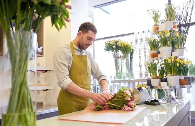 Homme en tablier préparant un bouquet de fleurs dans une boutique lumineuse et accueillante