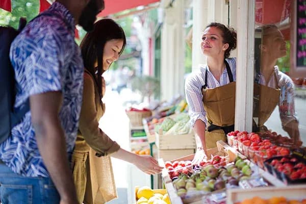 clients échangeant avec une vendeuse dans un marché de fruits ensoleillé