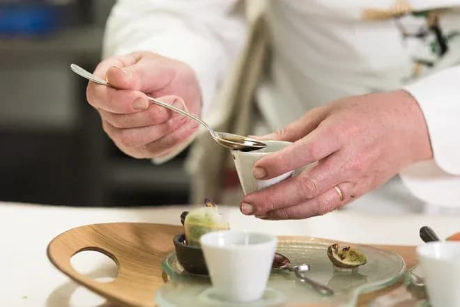 Chef en train de dresser un plat avec une cuillère et des petites verrines sur un plateau.
