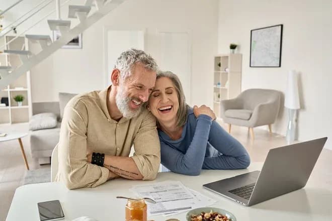 couple souriant assis à une table avec un ordinateur portable et des documents devant eux