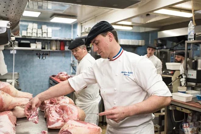 charcutier en blouse blanche découpe des morceaux de porc dans un atelier de boucherie