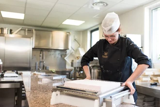 artisan confiseur en train de couper une préparation sucrée dans une cuisine professionnelle
