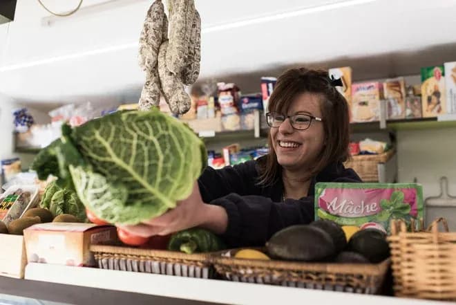 épicière souriante tend un chou vert sur le comptoir avec saucissons et légumes