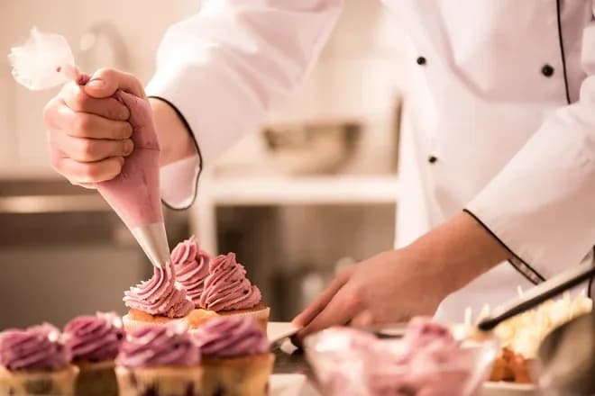pâtissier décorant des cupcakes avec de la crème rose à l'aide d'une poche à douille