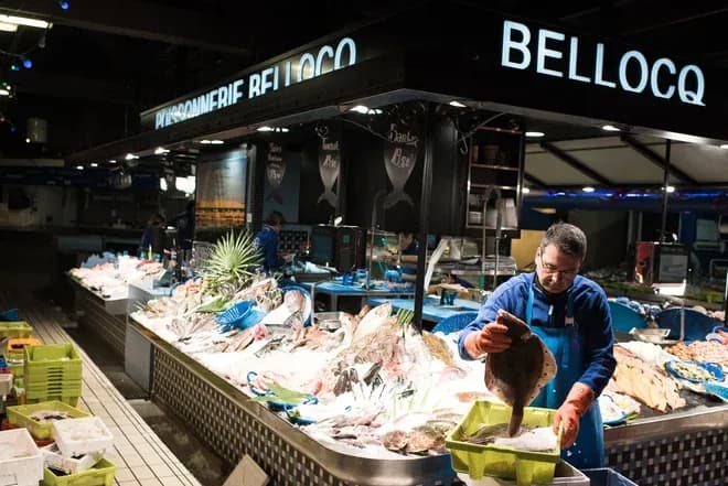 Vendeur de poisson préparant des produits de la mer sur un étal bien garni dans un marché.