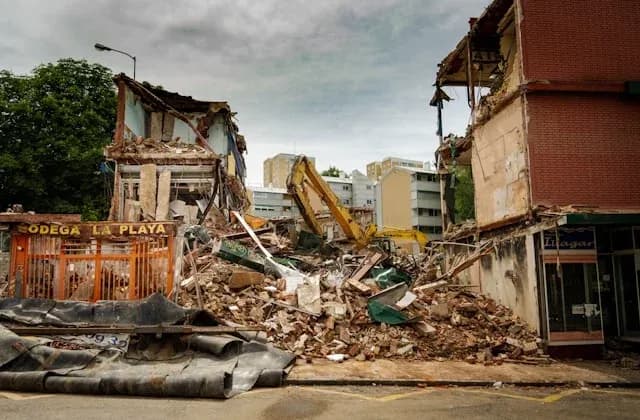 bâtiment effondré avec débris sur la route et une pelleteuse en arrière-plan