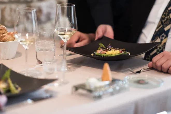 plat gastronomique servi sur une assiette noire avec des verres et du pain en arrière-plan