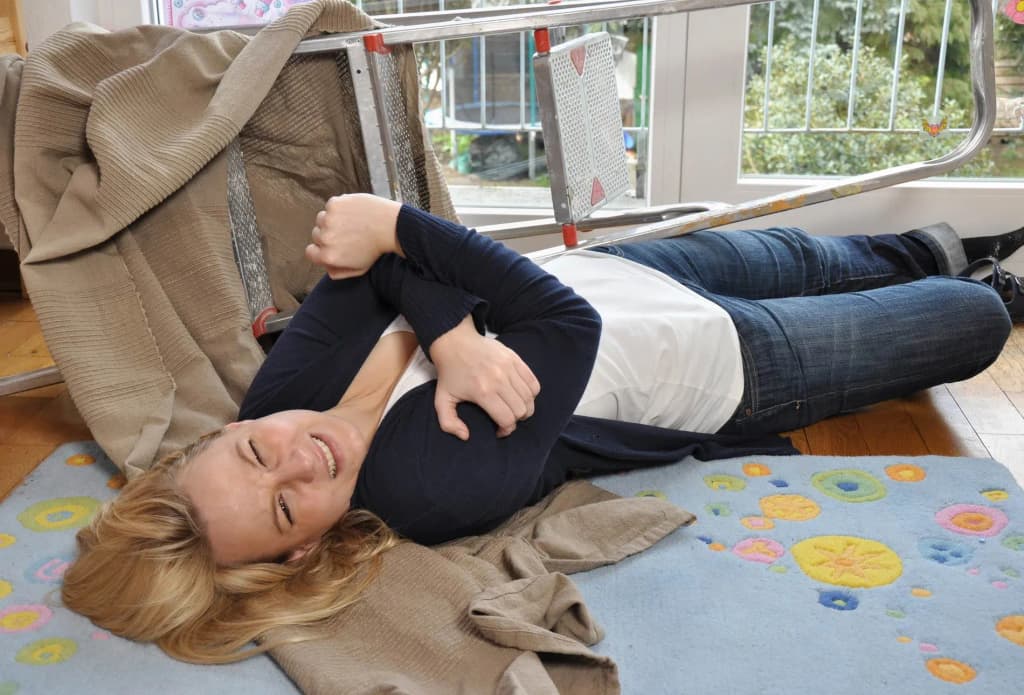 femme allongée au sol avec un bras replié près d'une échelle renversée et un tapis coloré