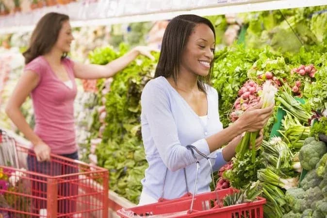 femme souriante choisissant des légumes frais dans un supermarché avec une autre personne en arrière-plan
