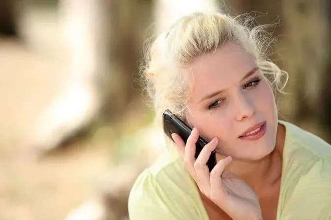 femme blonde au téléphone dans un environnement naturel avec un air pensif